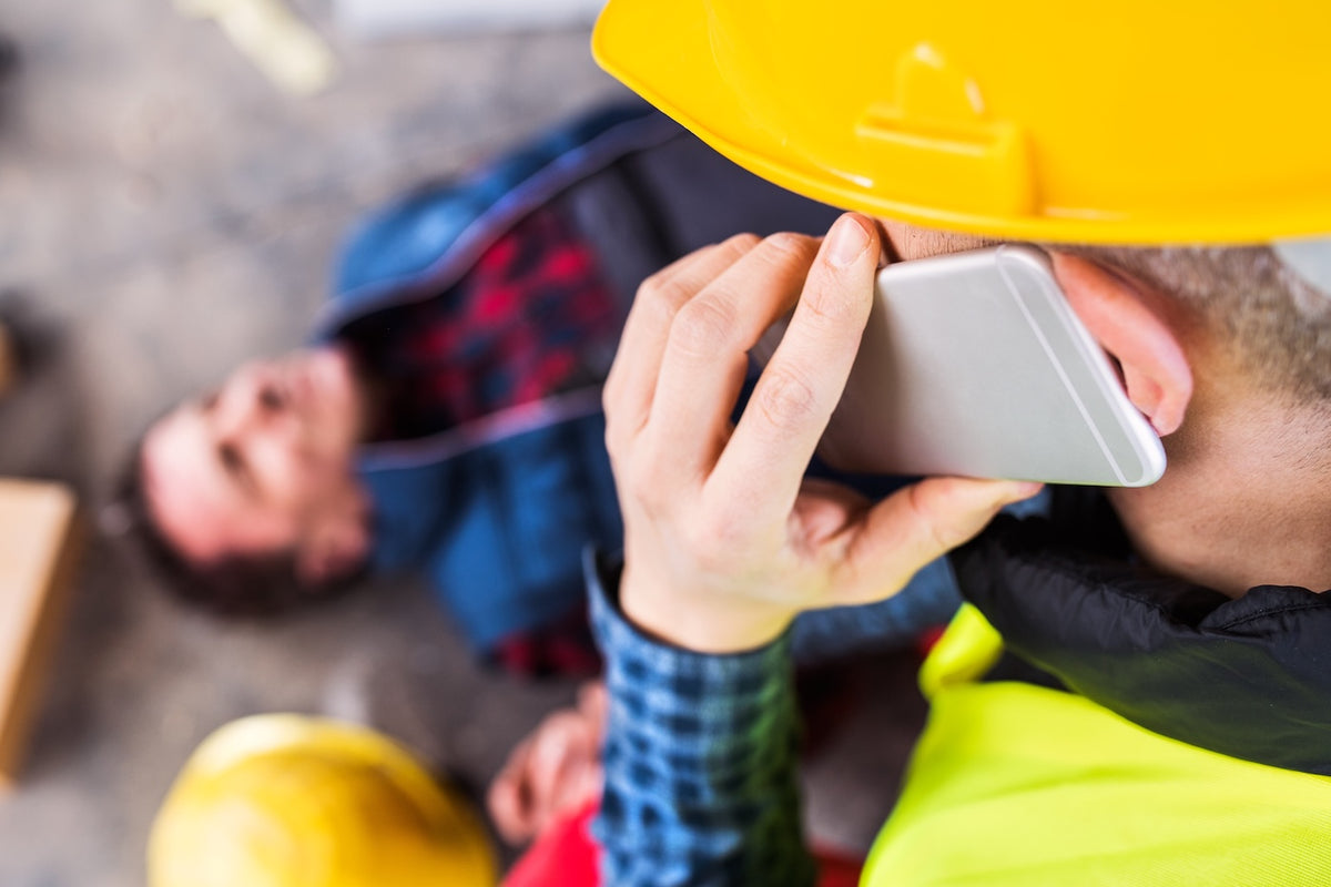 Person in a hard hat talking on a phone with another person in the background.
