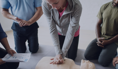 Person performing CPR on a mannequin with others observing.